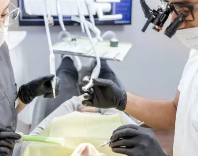 Nova-Smile Praxis in Düsseldorf-Mörsenbroich: Behandler mit Lupenbrille führt Kariesbehandlung durch, zwei Fachpersonal in weißen Kitteln arbeiten am Patienten.